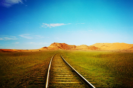 gray train way between green field during daytime thumbnail
