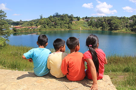 four toddlers sitting on rock infront of body of water at daytime thumbnail