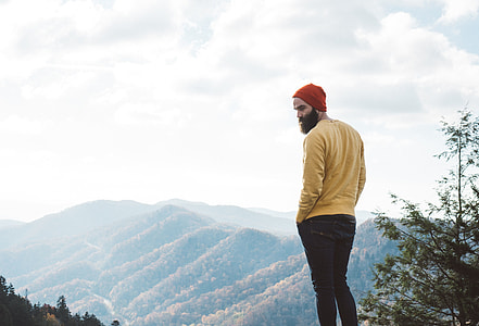 A man with a beard and hat near mountains thumbnail