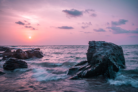 timelapse photo of sea waves crashing on grey stones at sunset thumbnail