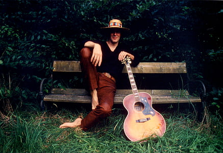 man in black long-sleeved shirt and brown pants sitting on brown wooden bench with guitar thumbnail