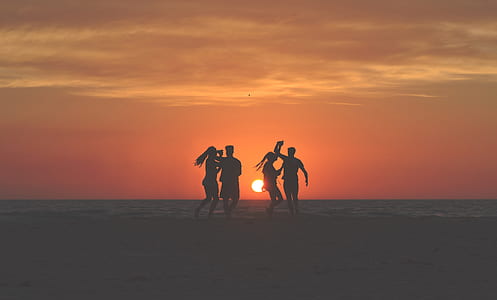 silhouette of four person on beach shore under orange sunset thumbnail