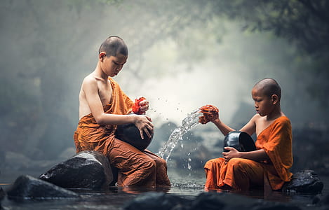 two children in orange dresses sitting on black rock thumbnail