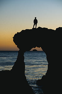 silhouette photograph of man standing on rock formation thumbnail