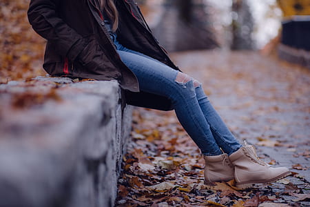 person wearing blue denim distress pants sitting on gray fence thumbnail