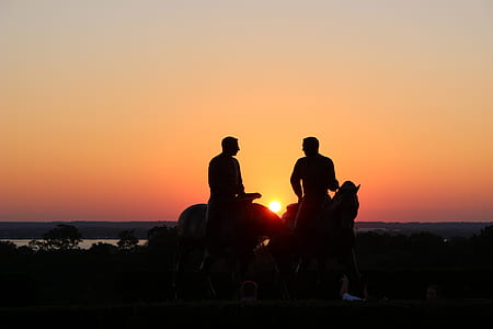 silhouette photo of 2 men riding on brown horses during sunset thumbnail