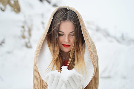 shallow focus photography of woman in brown coat holding snow thumbnail
