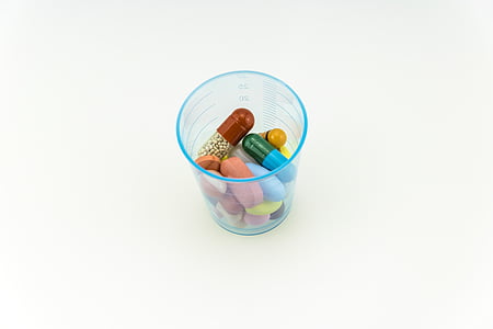 assorted-color capsules and tables on blue plastic cup on white surfacxe thumbnail