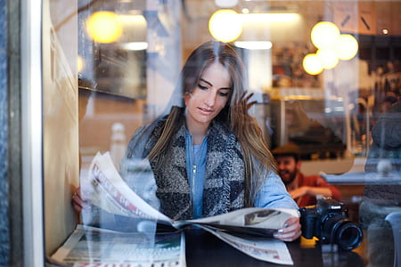woman reading newspaper in front of cafe window thumbnail