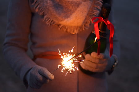 close up photo of person holding lit sparkler and wine bottle thumbnail