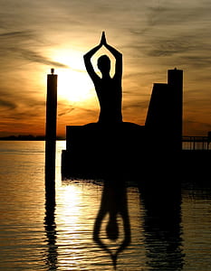 silhouette of person standing on body of water with dance gesture during golden hour thumbnail
