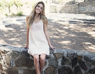 woman in white dress sitting on rock fence thumbnail