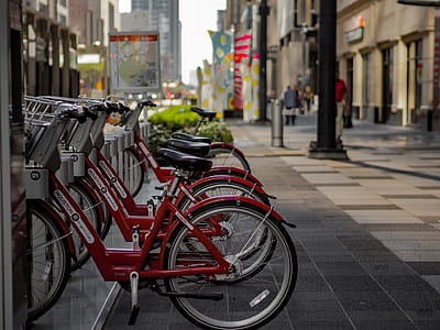 red city bikes parked near black pole between concrete buildings thumbnail