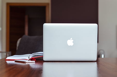 silver MacBook on brown wooden table beside pen and book thumbnail