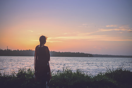 woman standing alone facing sea under orange sky thumbnail