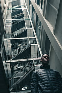 man wearing black bubble jacket standing in between high rise buildings thumbnail