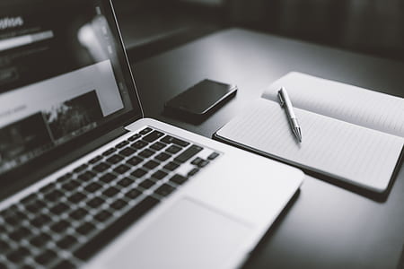 Gray Scale Photography of Macbook Iphone Notebook on Table thumbnail