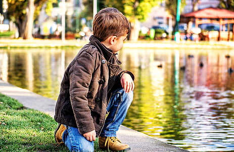 boy kneeling on green grass beside body of water at daytime thumbnail