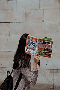 woman standing beside concrete wall while covering her face with book thumbnail