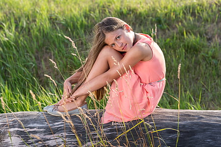 girl wearing pink sleeveless dress sitting on brown trunk tree thumbnail