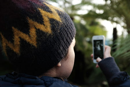 close-up photo of boy wearing knitted cap capturing green plants thumbnail