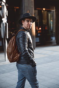 man in black leather jacket wearing brown leather backpack walking on street during daytime thumbnail