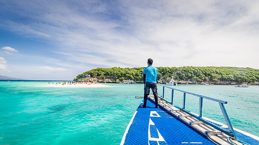 man standing on boat facing islet thumbnail