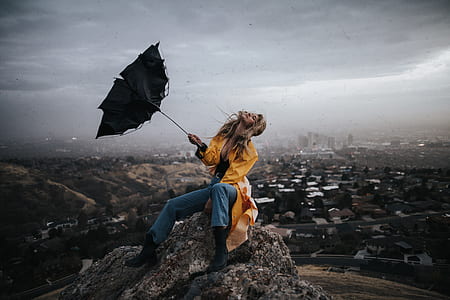 woman sitting on rock with her umbrella being blown away thumbnail