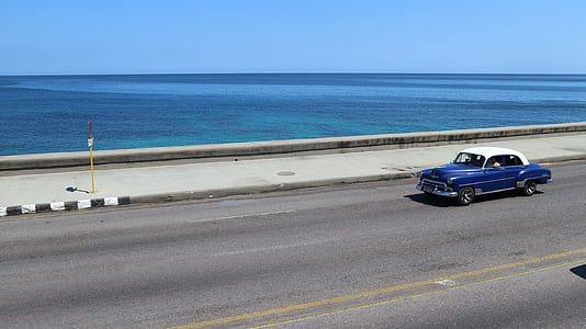 classic blue vehicle passing beside body of water during daytime thumbnail