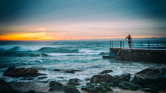 man standing on concrete dock beside seawave at daytike thumbnail