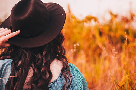 woman wearing teal and gray striped top and black cowboy hat looking at brown grass field selective focus photography thumbnail