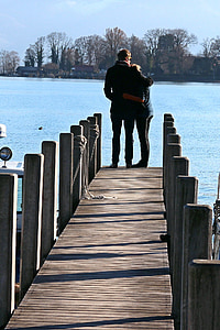 man hand over woman's shoulder standing on dock facing body of water thumbnail