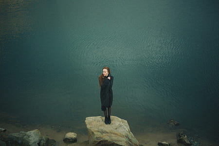 woman standing on rock near body of water thumbnail