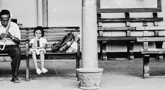 grayscale photography of child sitting on chair beside man holding umbrella thumbnail