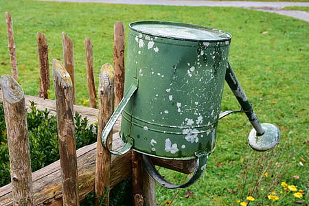 green steel watering can on brown wooden fence thumbnail