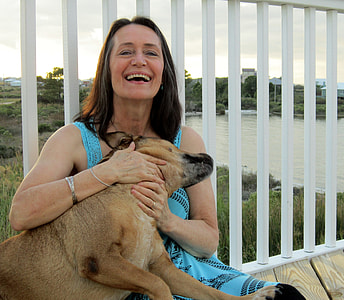 woman sitting on gray wooden floor while cuddling with brown dog during daytime thumbnail