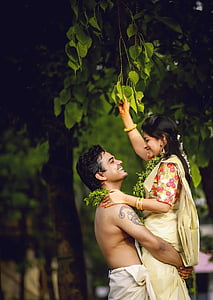 smiling topless man carrying woman underneath green leafed tree during daytime thumbnail