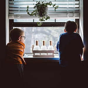 two boys standing beside window during daytime thumbnail