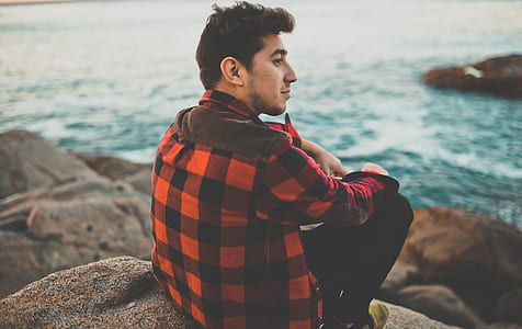 person sitting on rock in front of body of water thumbnail