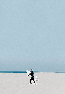 man wearing black wetsuit holding white surfboard walking on shoreline thumbnail
