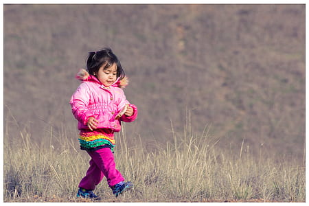 Woman in Pink Down Jacket Walking on Green Grass during Daytime thumbnail