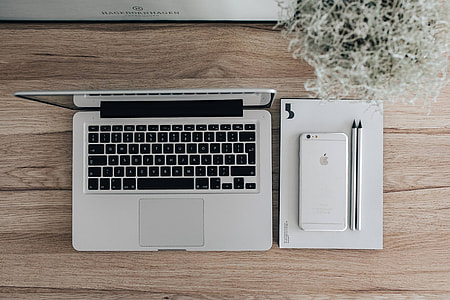 Silver Acer laptop on a wooden desk with a green plant, pencils and an Apple iPhone thumbnail
