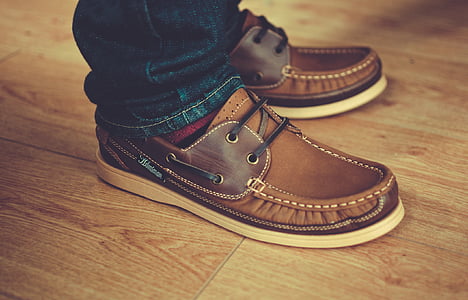 person wearing pair of brown boat shoes standing on brown wooden floor thumbnail
