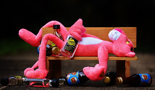 pink panther plush toy laying on brown wooden bench near liquor bottles thumbnail