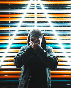 man wearing gray zip-up hoodie covering his face behind white LED light thumbnail