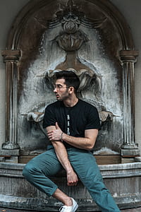 man in black shirt and teal pants sitting on fountain thumbnail