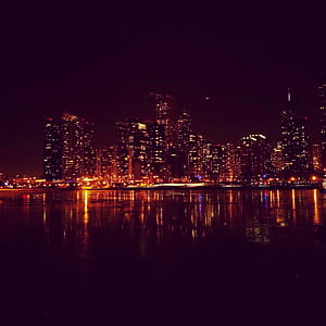 lightened city buildings beside body of water at night time thumbnail