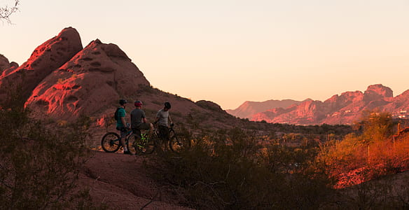 three men with bicycles standing near mountain during daytime thumbnail
