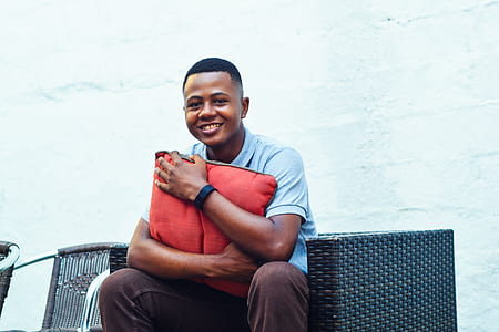 man wearing gray shirt holding red pillow sitting on black sofa thumbnail