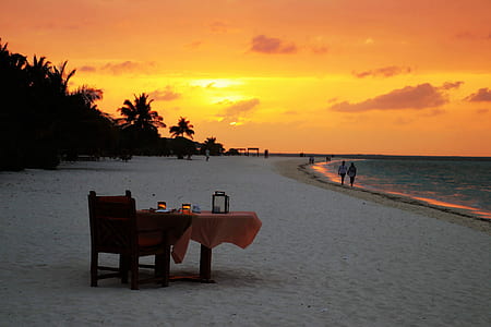 brown wooden armchair with table on seashore during golden hour thumbnail